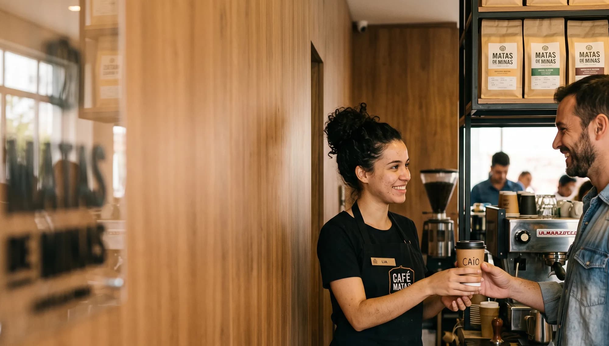 Barista sorridente entregando um copo com o nome do cliente na cafeteria